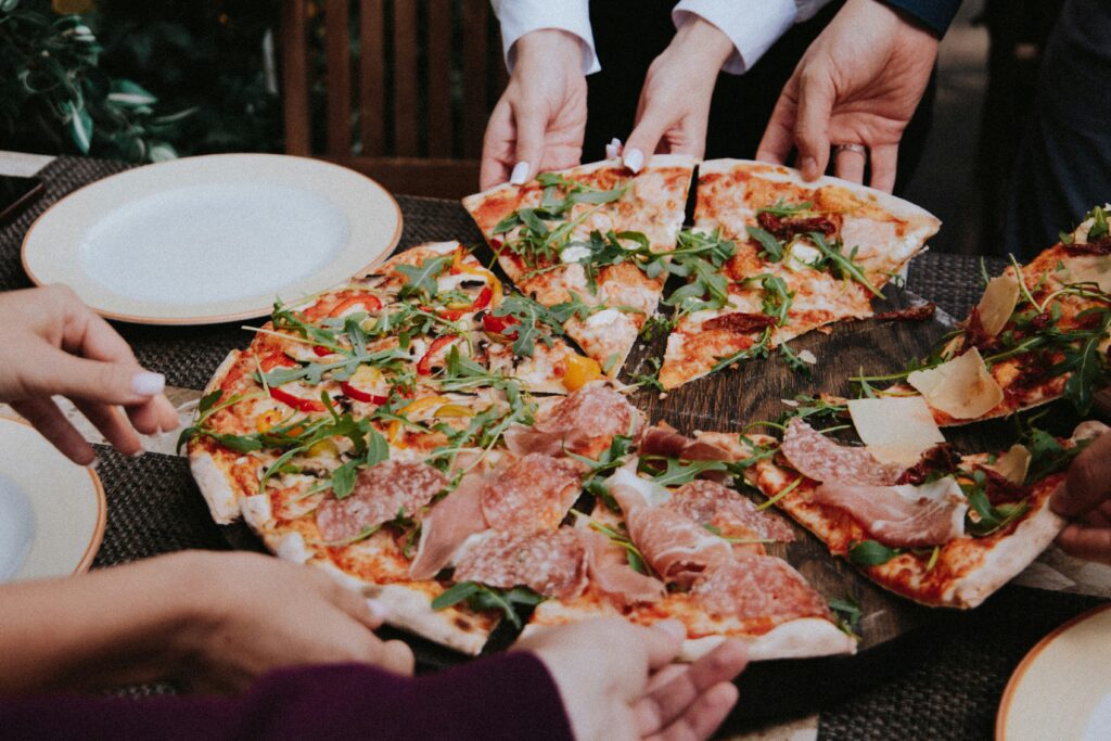 Several hands take pizza slices from a large plate