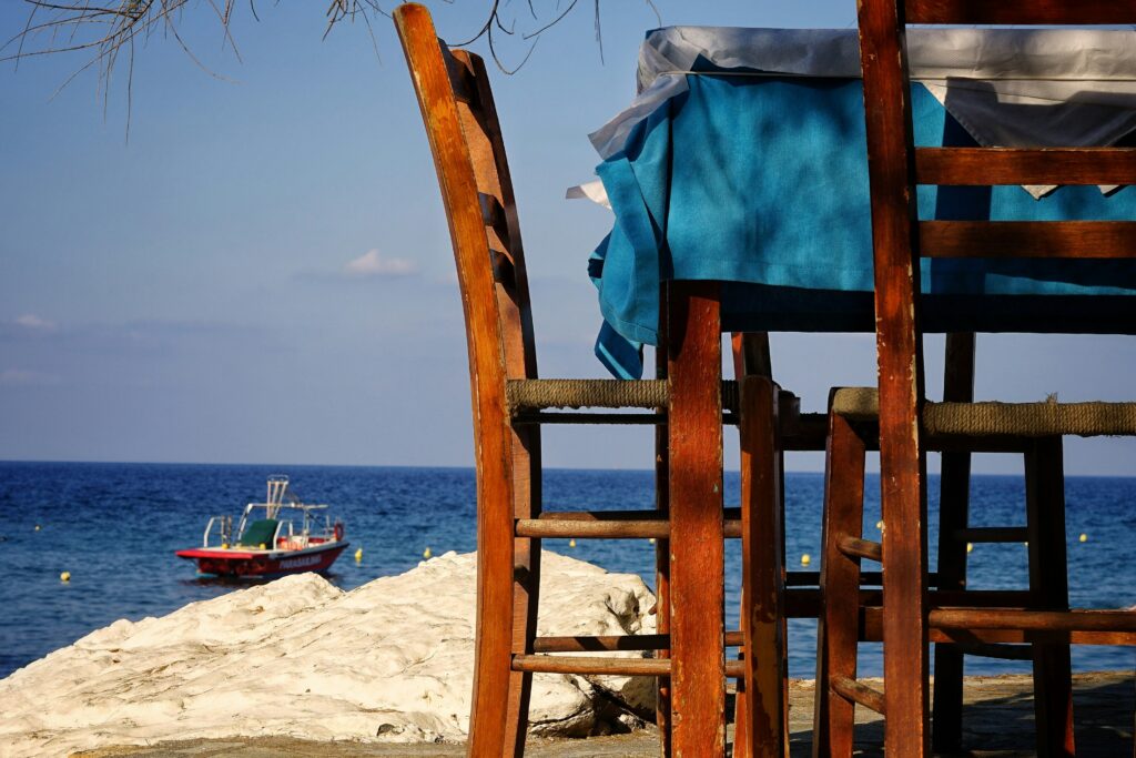 Two wooden chairs and a table with sea and a boat in the background